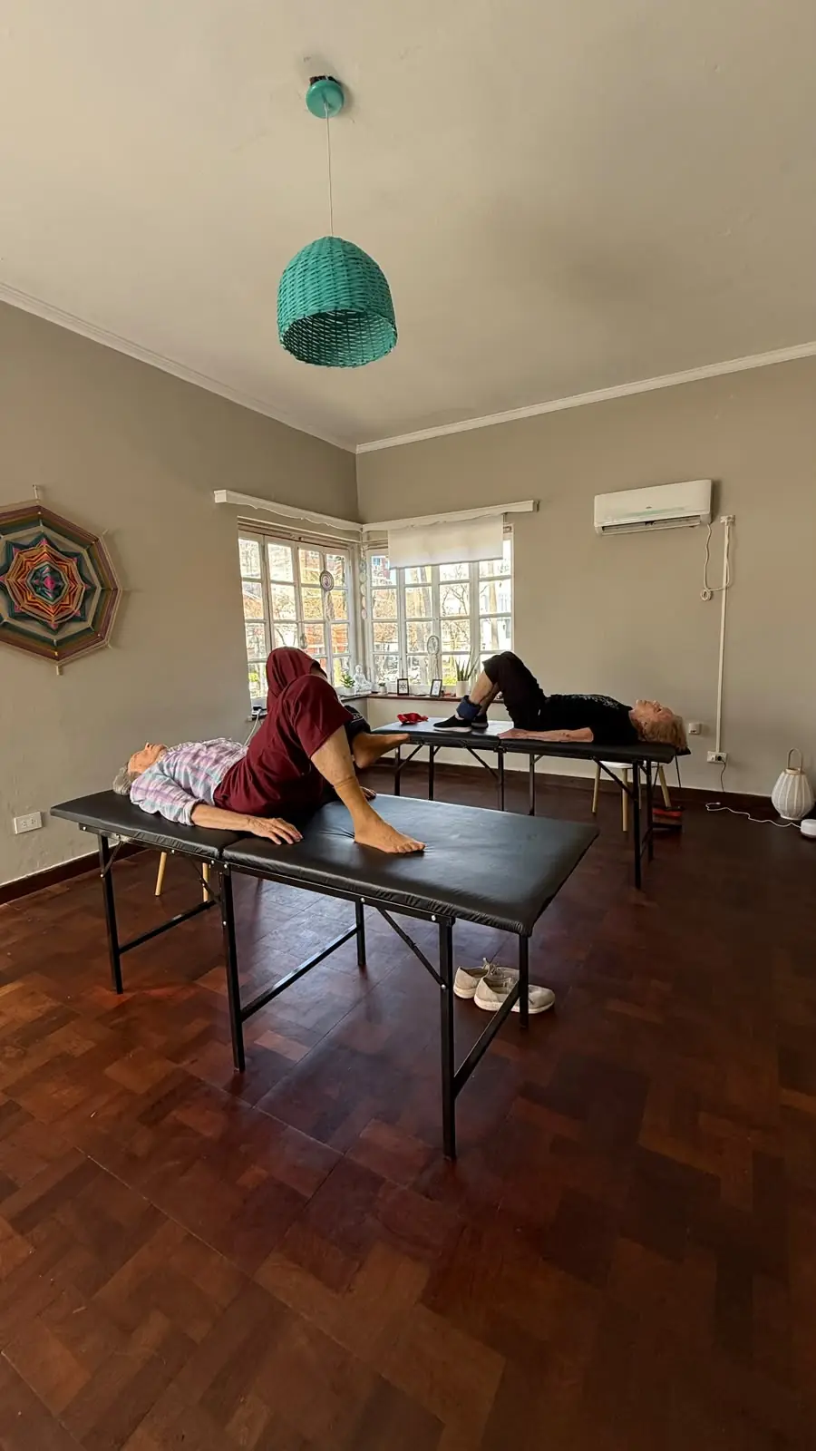 Dos personas entrenando las piernas en camilla, en una sala luminosa