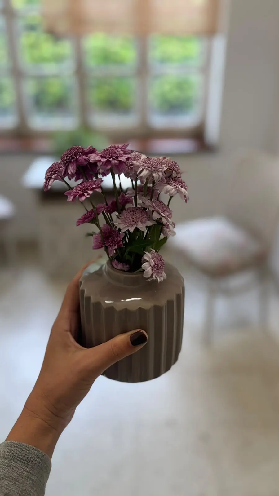 Una mano sostiene un florero con flores lilas en el consultorio