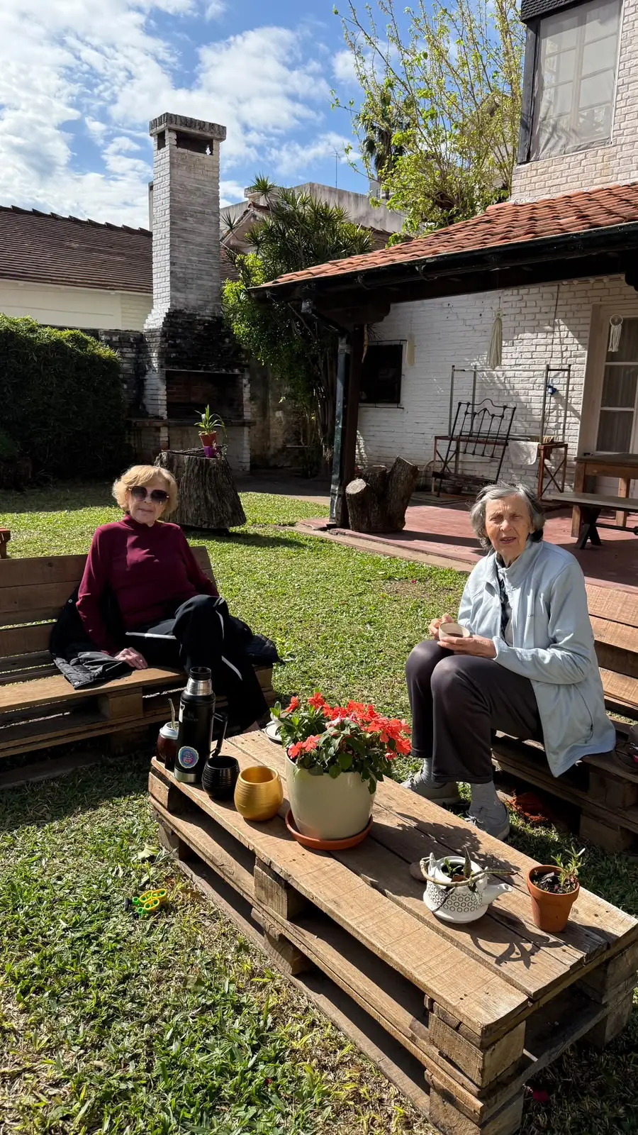 Dos personas sentadas en el jardín compartiendo un mate